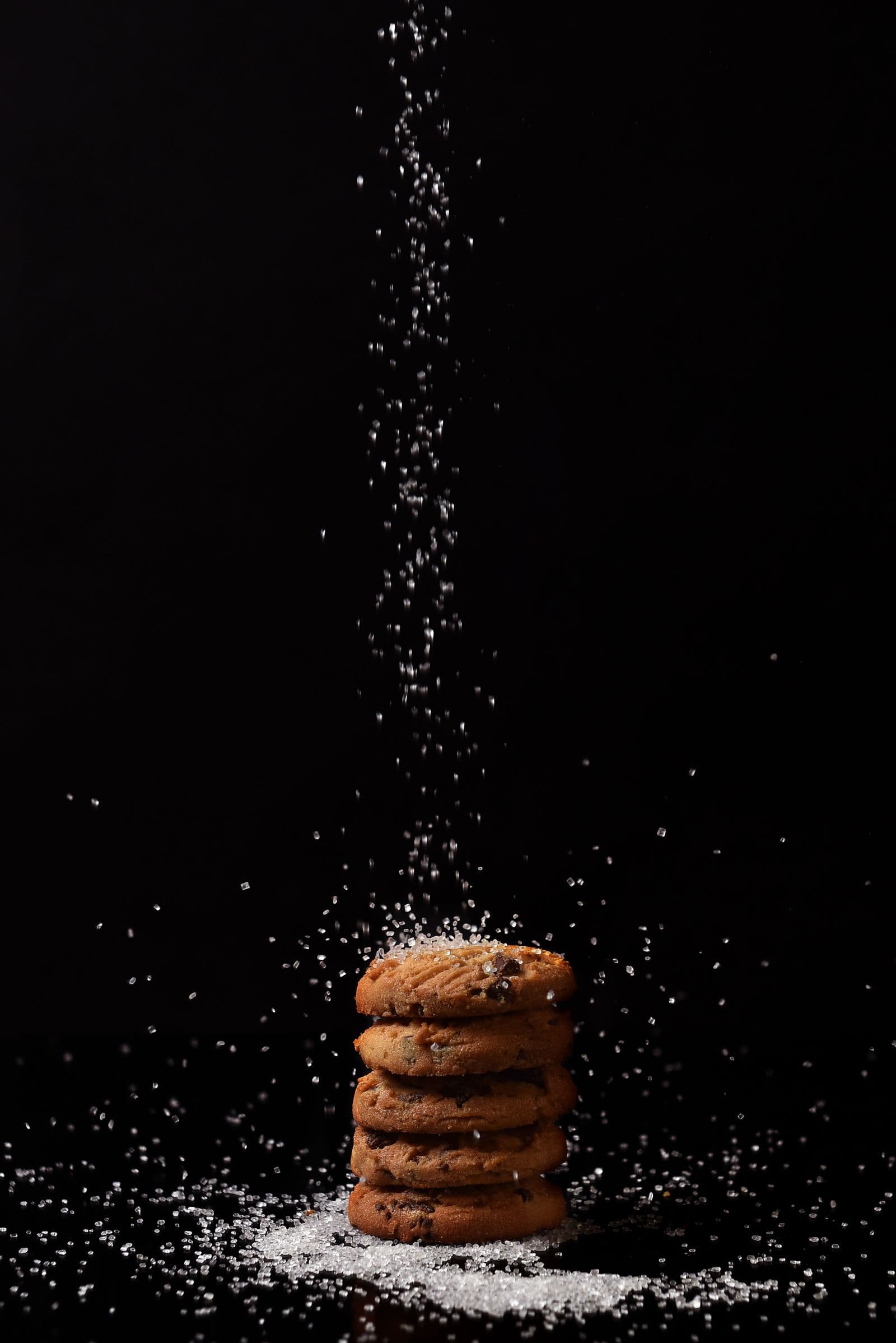 A stack of cookies on a dark surface with sugar falling around them