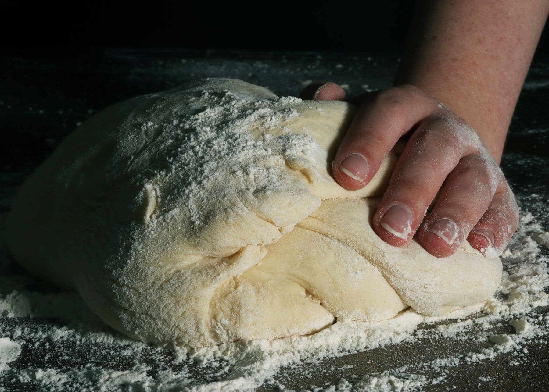 Hands working dough on a floured surface