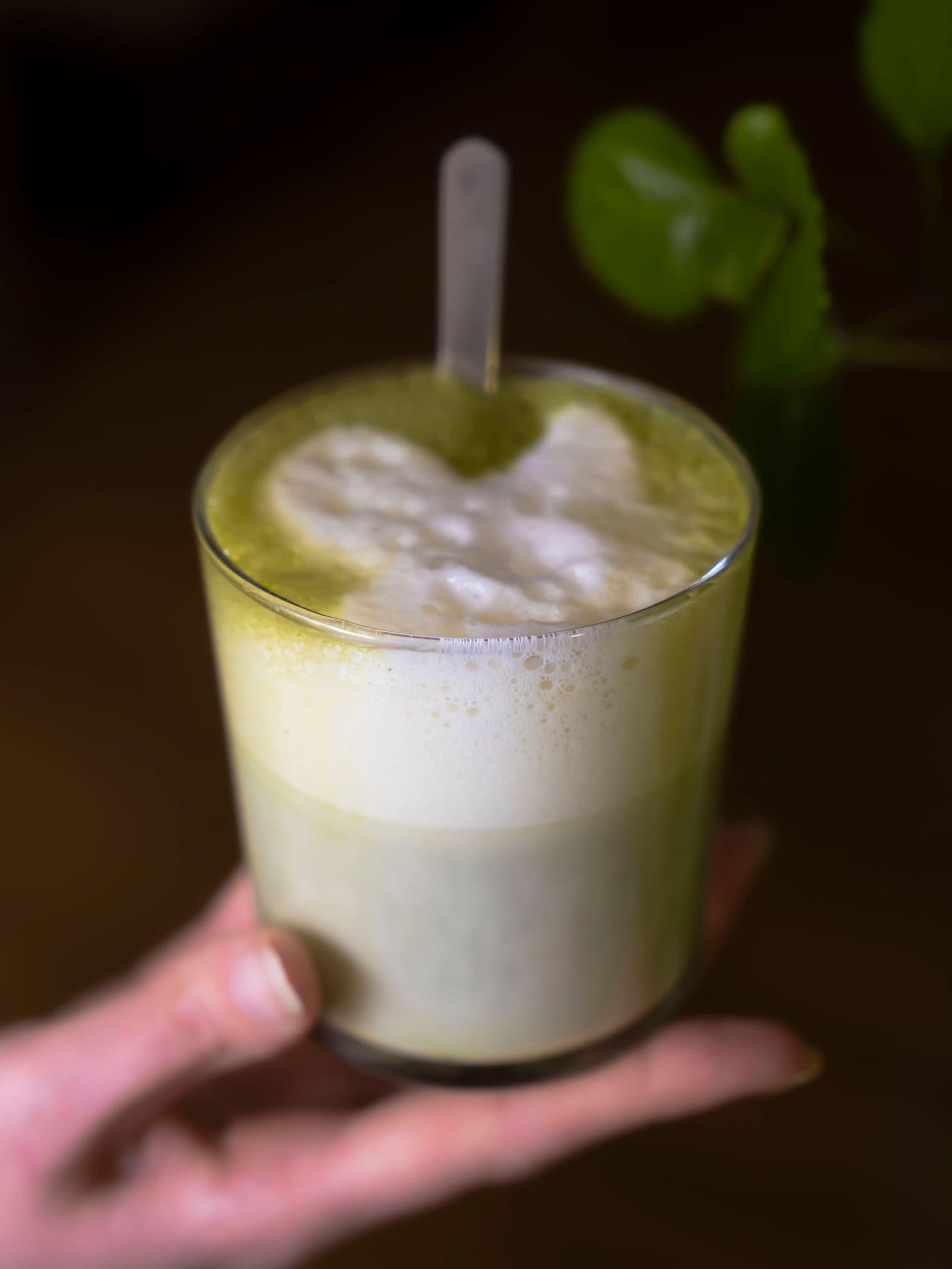 A hand holding a glass of frothy green matcha